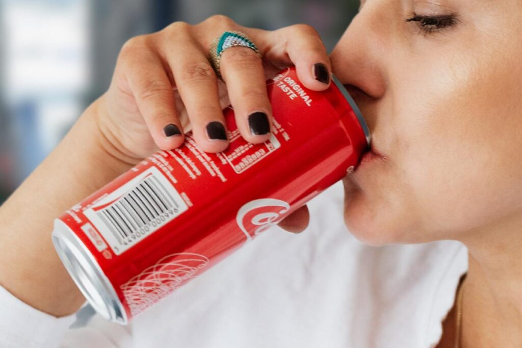 Donna che beve una lattina di coca cola per strada