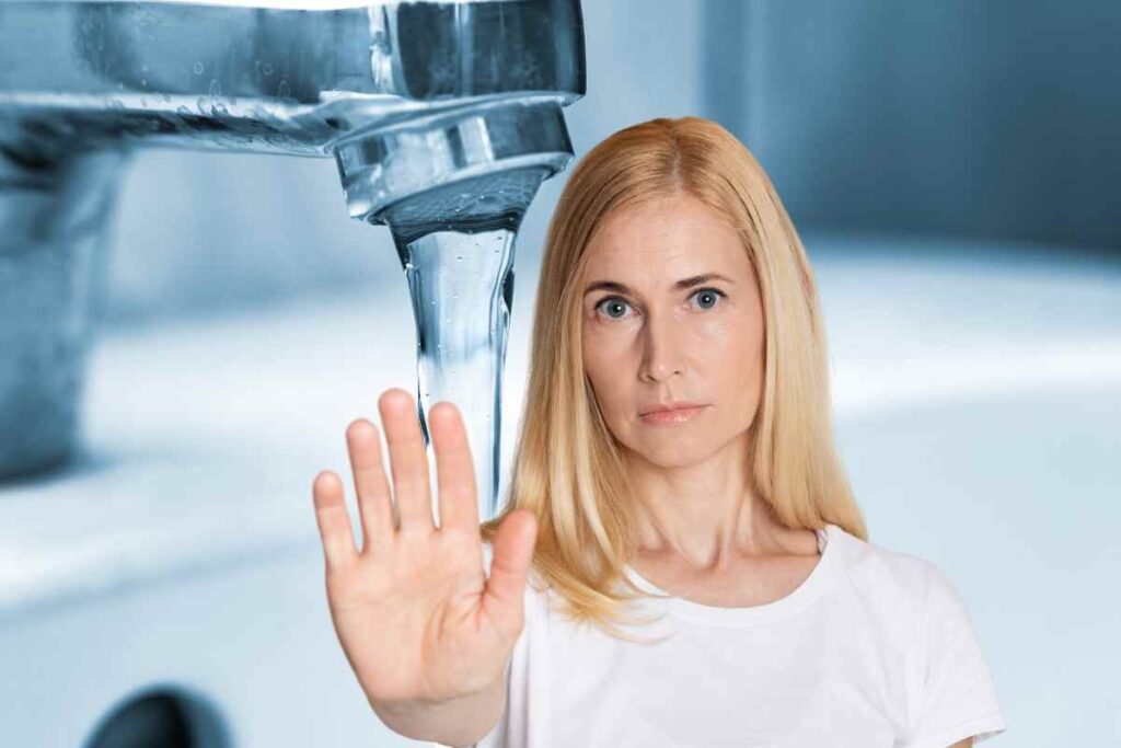Rubinetto con acqua e donna con mano in avanti
