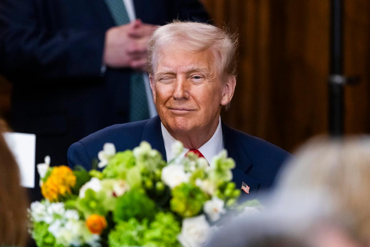 donald trump seduto ad un tavolo che strizza l'occhio e davanti a lui dei fiori