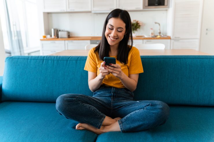 Ragazza seduta sul divano che svuota il cestino di WhatsApp dal suo smartphone