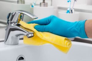 Mano con guanto azzurro pulisce rubinetto con panno in microfibra giallo
