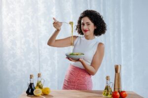 Ragazza con piatto di pasta e una forchetta in mano