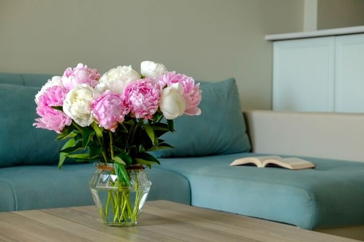 Vasetto in vetro con fiori di peonie sul tavolo davanti al divano