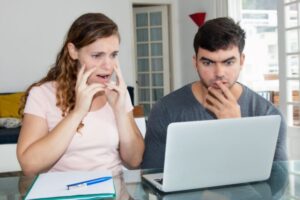 uomo e donna seduti davanti al computer con espressione preoccupata