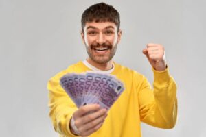 uomo che sorride con tante banconote da 500 euro in una mano