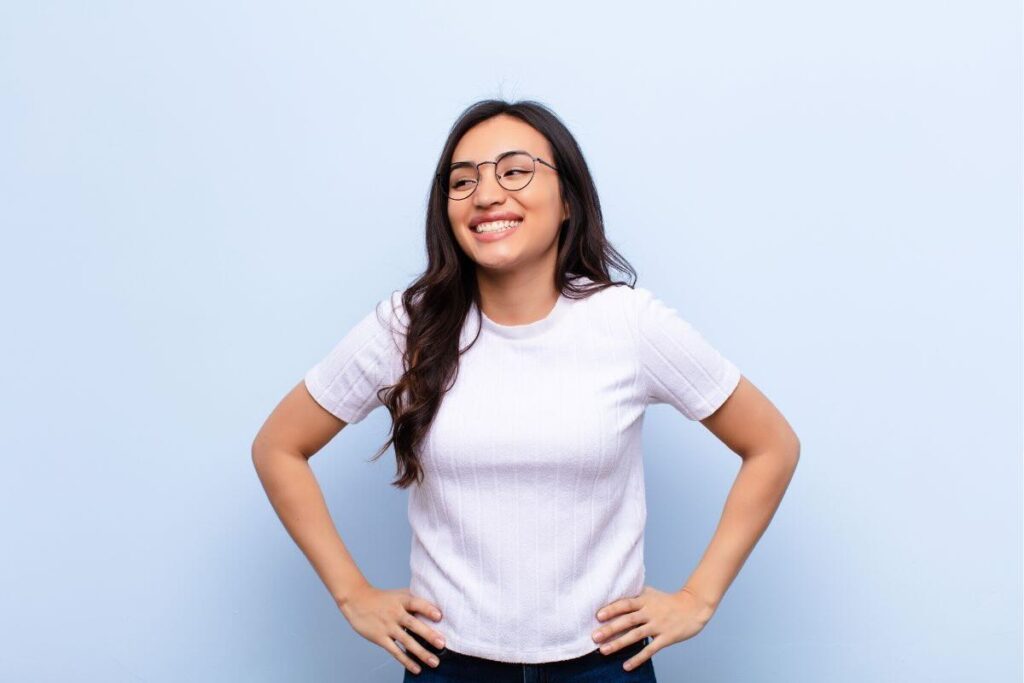 Ragazza con t-shirt bianca e occhiali da vista, sorridente, mani sui fianchi