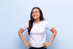Ragazza con t-shirt bianca e occhiali da vista, sorridente, mani sui fianchi